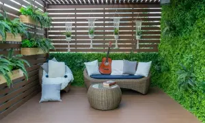 Un piccolo terrazzo coperto arredato con divanetto in vimini, poltrona, tavolino, chitarra e piante. Idee per arredare un piccolo terrazzo coperto.