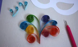 Creazione di una maschera carnevale fai da te con strisce di carta colorata arrotolate e uno strumento per quilling.