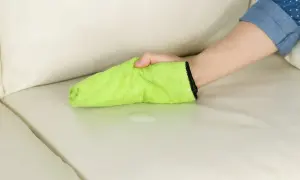 Mano che pulisce una macchia di liquido su un divano chiaro con un panno verde. La birra macchia i vestiti, ma questo panno è pronto a salvare il divano.