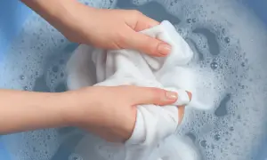 Mani che lavano un tessuto bianco in acqua saponata, creando schiuma e bollicine. L'acqua ossigenata sui tessuti aiuta a sbiancare.