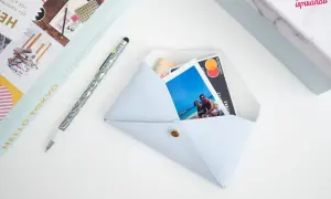 Pochette fai da te azzurra, con foto di coppia, carta di credito e banconota. Accanto, una penna e un libro.