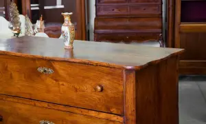 Cassettiera in legno scuro, oggetto di **ristrutturazione mobili antichi**, con vaso decorato e modellini di navi sullo sfondo.