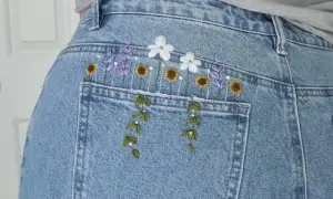 Top di jeans fai da te con ricamo floreale: lavanda, girasoli e margherite adornano la tasca posteriore, creando un look unico e primaverile.