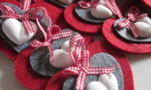 Cuori natalizi fai da te con feltro rosso e grigio, cuori bianchi e nastri a quadretti rossi.