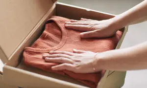 Mani che accarezzano una maglietta color terracotta appena arrivata, pronta per il primo lavaggio per fissare i colori.