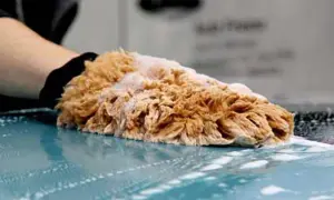 Mano con guanto nero lava un'auto con una spugna soffice, mostrando diversi tipi di orlo a macchina.