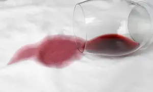 Calice di vino rosso rovesciato su tessuto bianco, creando una macchia. Come togliere macchie sconosciute e ostinate.