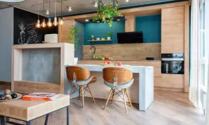 Cucina moderna con isola centrale e sedie in legno. L'arredamento mix and match crea un ambiente accogliente, con dettagli industriali e tocchi di colore vivace.