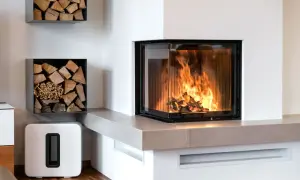 Un camino moderno con vetro angolare e fiamme vive, circondato da legna da ardere ordinata su mensole a muro.