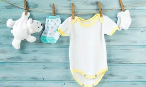 Vestiti da neonato bianchi e gialli appesi ad asciugare. Scopri come smacchiare i vestiti dei neonati ingialliti per mantenerli freschi.