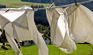 Capi ingialliti dal sole ondeggiano al vento su uno stendibiancheria, con un paesaggio verdeggiante e una casa sullo sfondo.