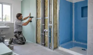Operaio fissa pannelli di cartongesso su struttura metallica, creando una nuova parete in un bagno in fase di ristrutturazione.