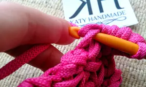 Mano che lavora all'uncinetto con filo rosa acceso, creando un punto pieno. Un tutorial su come ricamare una stella a punto pieno.