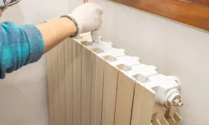 Mano con guanto bianco che applica vernici per termosifoni con un pennello. Il radiatore è beige e la vernice è bianca.
