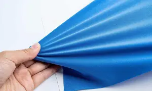 Mano che tiene un tessuto blu brillante, mostrando la sua elasticità e la trama del punto elastico a mano.