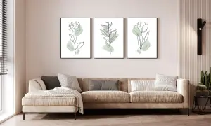 Divano beige in un soggiorno al piano terra poco luminoso, con tre quadri botanici minimalisti e una lampada da parete.