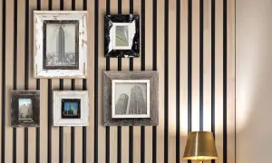 Vari tipi di cornici per quadri, con finiture in legno grezzo e bianco anticato, incorniciano immagini di grattacieli su una parete a listelli.