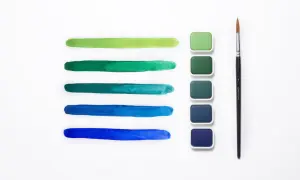 Pennellate verdi e blu mostrano la differenza tra colori acrilici e tempere, con pastiglie di colore e un pennello.