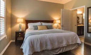 Accogliente camera da letto colori caldi, con letto king size, comodini con lampade e porta aperta su un bagno.