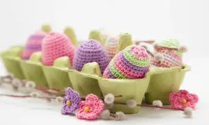 Uova di Pasqua all'uncinetto in lana colorata, perfette per lavoretti di Pasqua creativi. Fiori e ramoscelli di salice completano la scena.