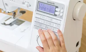 Dito, una mano seleziona tra i tanti punti macchina da cucire disponibili su un display digitale.