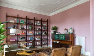 Soggiorno accogliente con **caldi colori pareti** rosa cipria, libreria a giorno piena di libri e oggetti, divano verde, poltrone in pelle e mobile vintage.