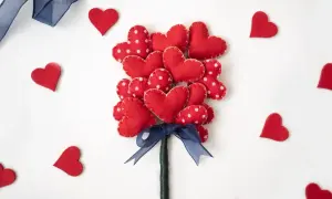 Un bouquet di cuori rossi in feltro, perfetti per regali fai da te San Valentino. Un nastro blu lega il tutto, circondato da cuoricini sparsi.