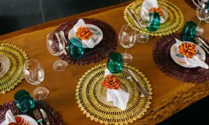Sottopiatti eleganti fai da te con decorazioni floreali arancioni, bicchieri verdi e posate su un tavolo di legno.