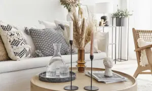 Tavolino rotondo con decanter, bicchieri, candele e scultura di testa. Cuscini decorativi e pampas sul divano creano un'atmosfera boho chic arredamento.