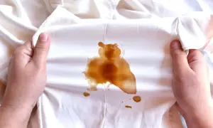 Mani che mostrano macchie di sapone marroni su un tessuto bianco.