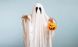Bambino con un lenzuolo bianco e occhi neri, pronto per raccogliere dolcetti con la sua zucca arancione. Un'idea per costumi halloween fai da te bambini.