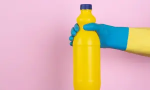 Mano con guanto blu e giallo tiene una bottiglia gialla. Attenzione, l'ammoniaca macchia i vestiti!