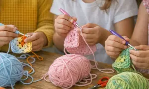 Bambini imparano come si ricama all'uncinetto, con gomitoli colorati e uncinetti.
