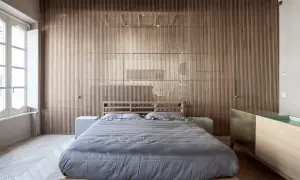 Camera da letto in stile giapponese con pareti in listelli di legno, letto basso con lenzuola grigie e un mobile in legno e ottone.