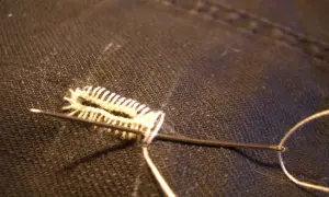 Un ago con filo bianco crea un punto occhiello a mano su tessuto scuro, un dettaglio di sartoria meticoloso.
