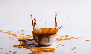 Schizzo di liquido marrone da una ciotola, creando macchie arancioni sui vestiti e sul tavolo.