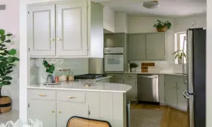 Cucina con mobili fai da te color salvia, piano bianco, elettrodomestici in acciaio e piante verdi.