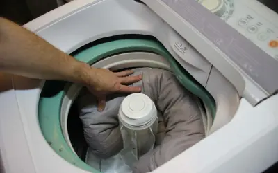 Mano che sistema la cuccia del cane nella lavatrice, pronta per essere lavata.