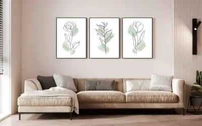 Divano beige in un soggiorno al piano terra poco luminoso, con tre quadri botanici minimalisti e una lampada da parete.