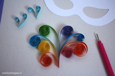 Creazione di una maschera carnevale fai da te con strisce di carta colorata arrotolate e uno strumento per quilling.