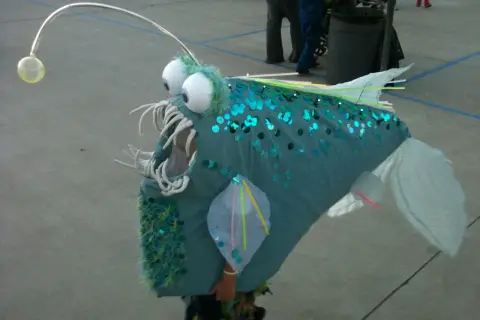 Un bambino indossa un costume da pesce lanterna fai da te, perfetto per un tema mare. Le paillettes blu e la canna da pesca con la luce lo rendono unico.
