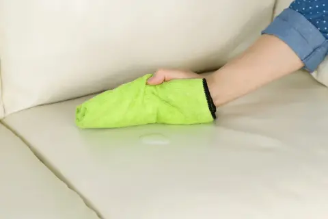 Mano che pulisce una macchia di liquido su un divano chiaro con un panno verde. La birra macchia i vestiti, ma questo panno è pronto a salvare il divano.