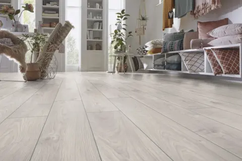 Un luminoso soggiorno con pavimento laminato effetto legno chiaro. Un divano con cuscini colorati e una libreria completano l'arredamento.