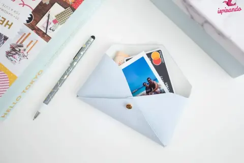 Pochette fai da te azzurra, con foto di coppia, carta di credito e banconota. Accanto, una penna e un libro.