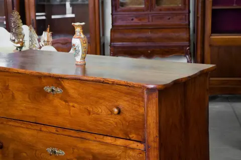 Cassettiera in legno scuro, oggetto di **ristrutturazione mobili antichi**, con vaso decorato e modellini di navi sullo sfondo.
