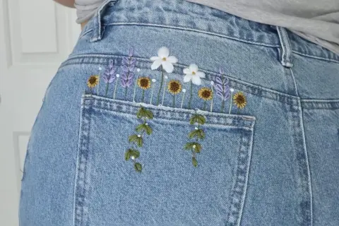 Top di jeans fai da te con ricamo floreale: lavanda, girasoli e margherite adornano la tasca posteriore, creando un look unico e primaverile.