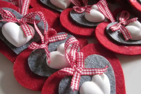 Cuori natalizi fai da te con feltro rosso e grigio, cuori bianchi e nastri a quadretti rossi.