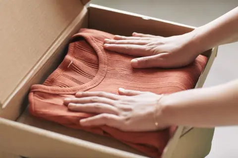 Mani che accarezzano una maglietta color terracotta appena arrivata, pronta per il primo lavaggio per fissare i colori.