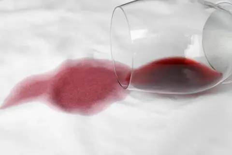 Calice di vino rosso rovesciato su tessuto bianco, creando una macchia. Come togliere macchie sconosciute e ostinate.