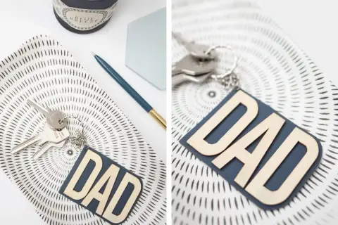 Portachiavi fai da te per la festa del papà con scritta "DAD" in legno su fondo blu. Un'idea regalo originale e personalizzata.